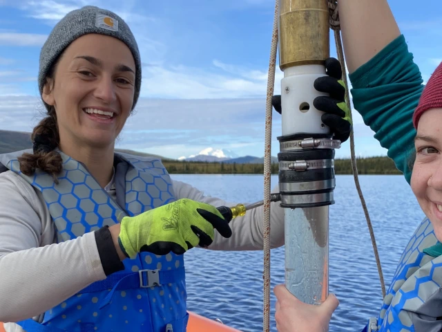 Sediment core tube held in a small boat on a lake.